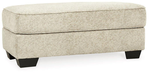 Stylish Monaghan Ottoman by Ashley Furniture with plush fabric and wooden legs, ideal for living room decor.