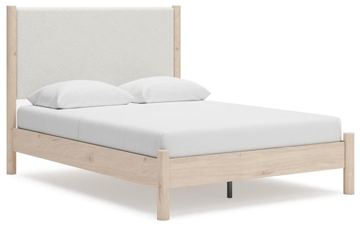 Ashley Furniture Cadmori upholstered bed with tan fabric and padded headboard, shown from a side angle in a well-lit bedroom setting.