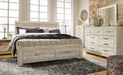 Ashley Furniture Bellaby Bed with upholstered headboard and wooden frame, shown in a cozy bedroom setting.