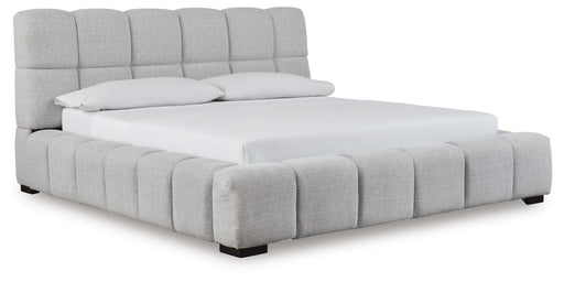 Ashley Furniture Grendusk upholstered bed with a tufted headboard and neutral fabric, shown from a side angle.