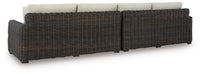 Ashley Furniture Kimora outdoor sectional with beige cushions and dark wicker frame, shown from the back.